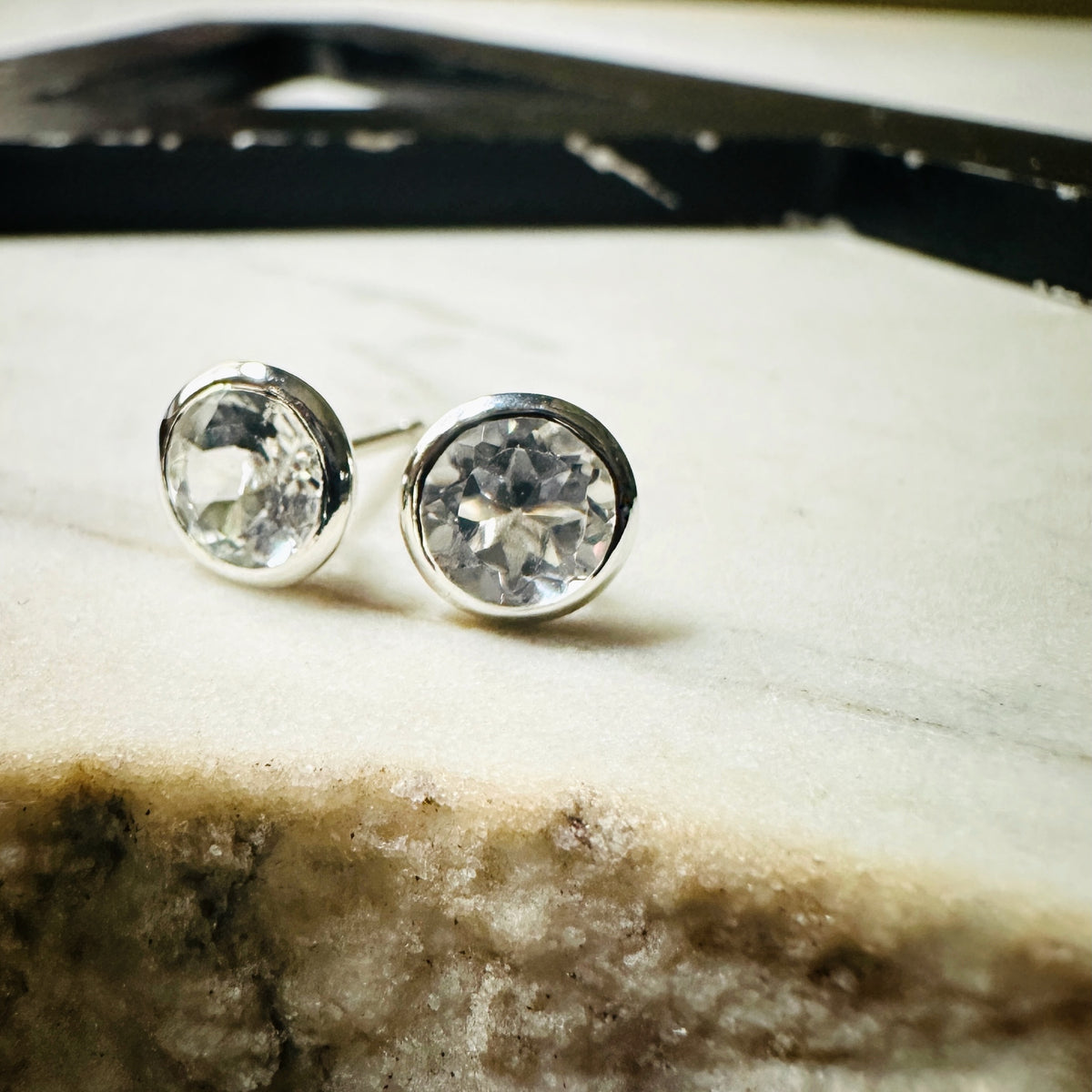 a pair of 6mm white topaz bezel set stud earrings resting on a marble surface