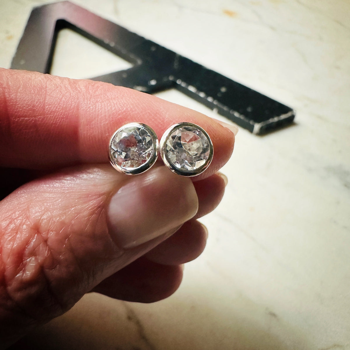 a pair of 6mm white topaz bezel set martini earrings in sterling silver being held in a hand for scale