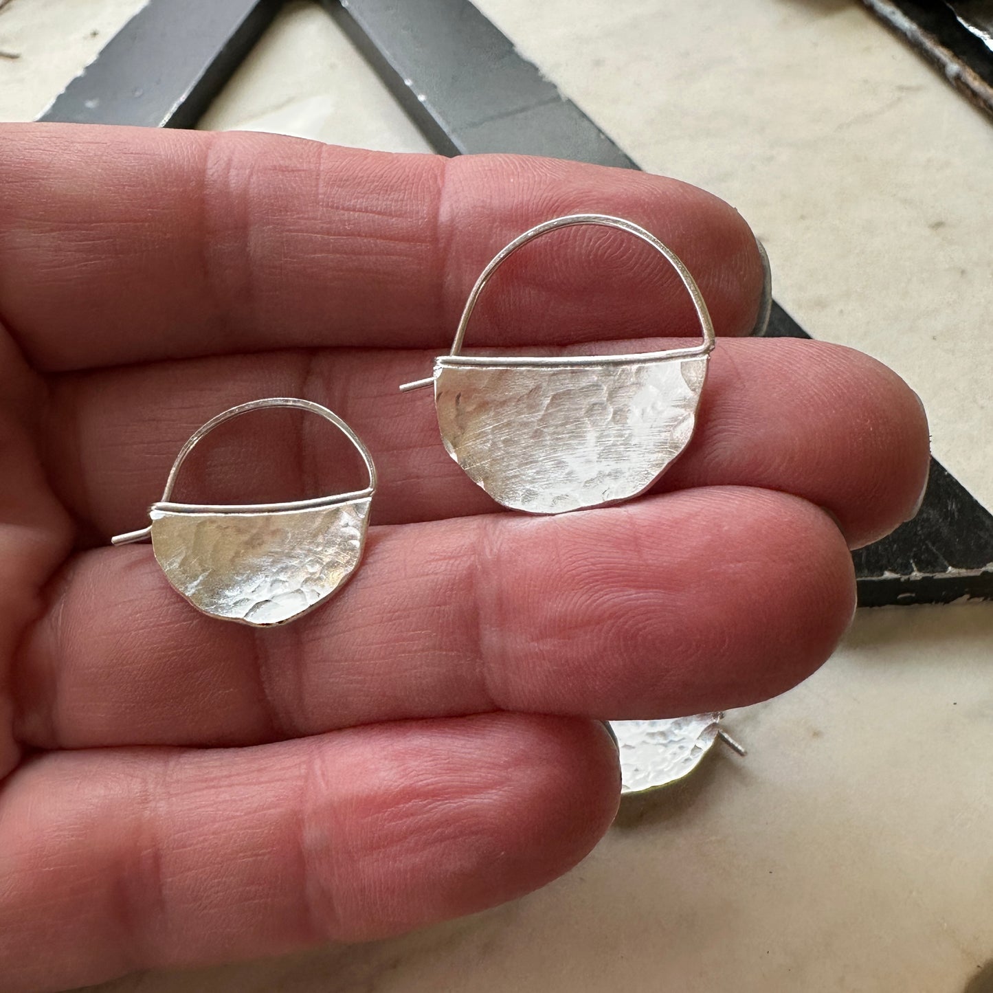 bright silver half circle hoop earrings, size small and medium shown on a hand for scale