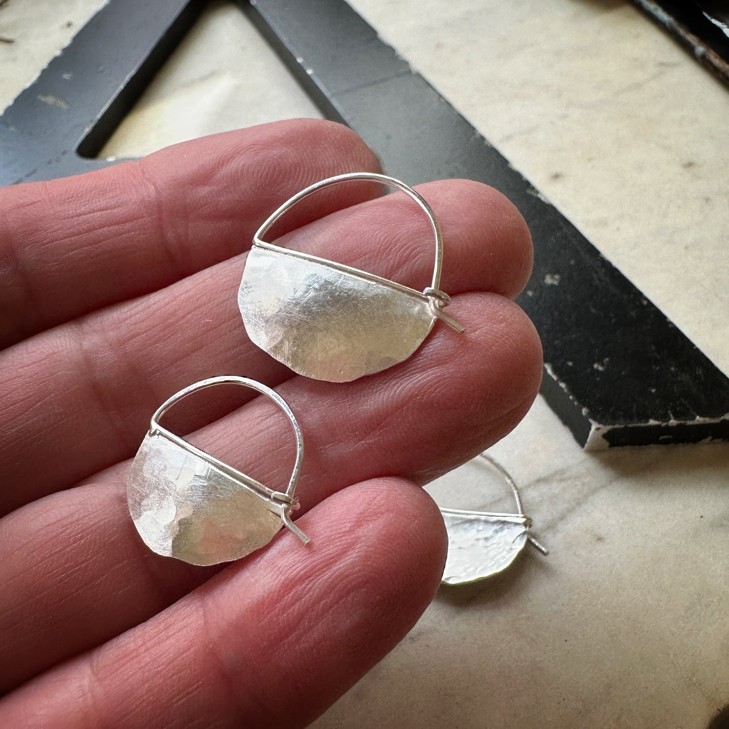 bright silver half circle hoop earrings, size small and medium from the back to show the clasp and on a hand for scale