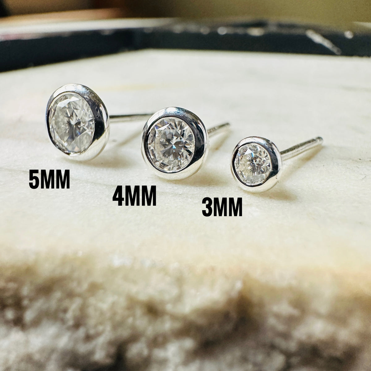 Size comparison between 3mm, 4mm and 5mm sterling silver Moissanite stud earrings n a marble slab