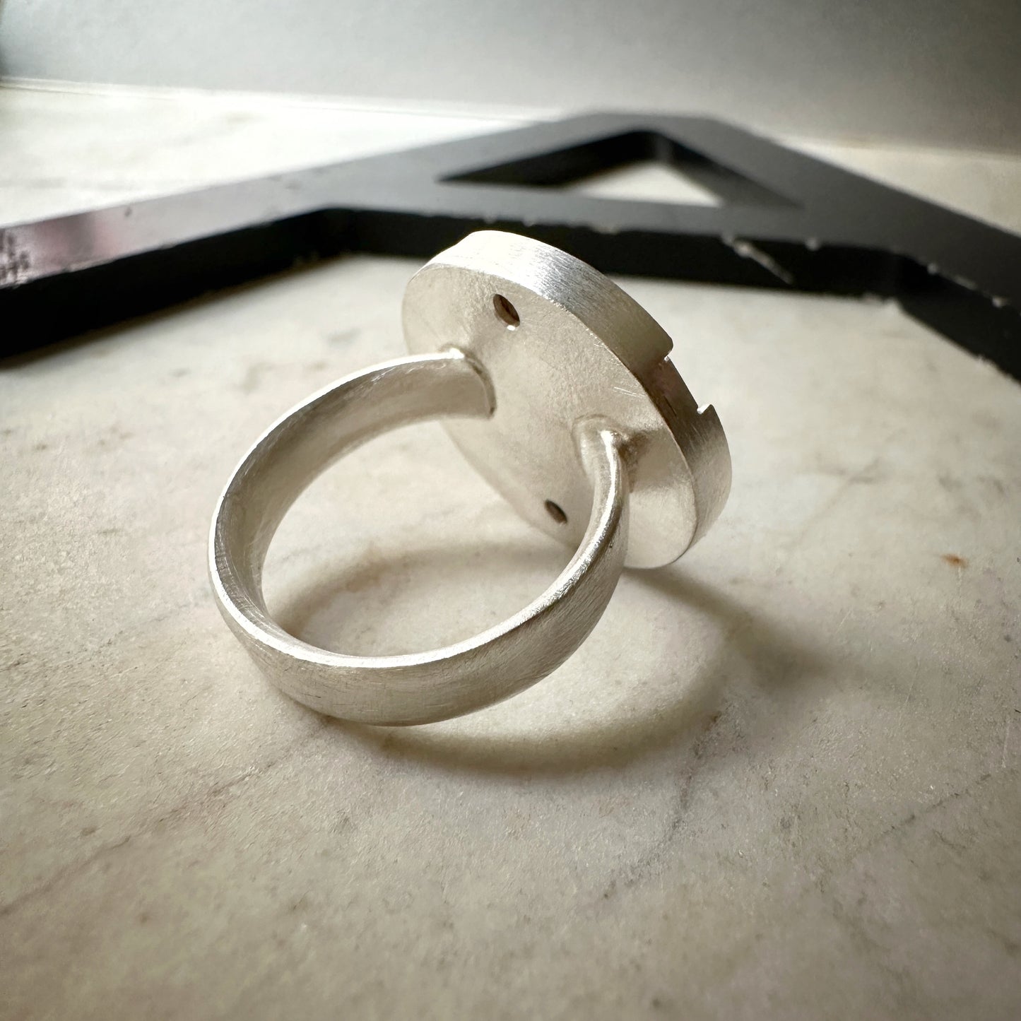 A sterling silver ring with a circular, disc-like back and a thick band, resting on a light marble surface.
