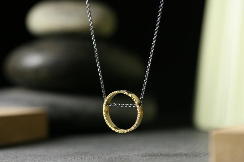 A half inch circle of 18k yellow gold hanging on a darkened silver chain that runs through the pendant.