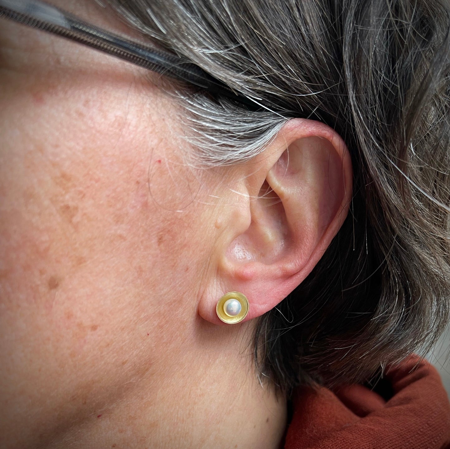 white pearls sit in yellow gold cups. shown in the ear for scale