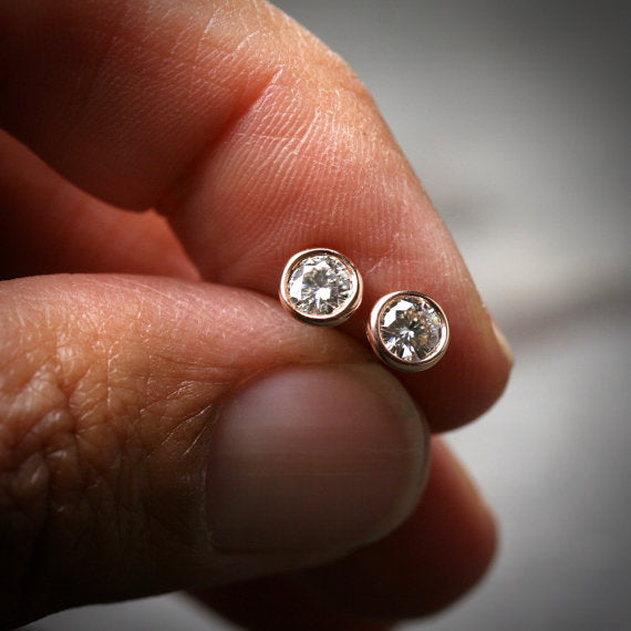 14k rose gold bezel set Moissanite stud earrings shown being held in a hand for scale