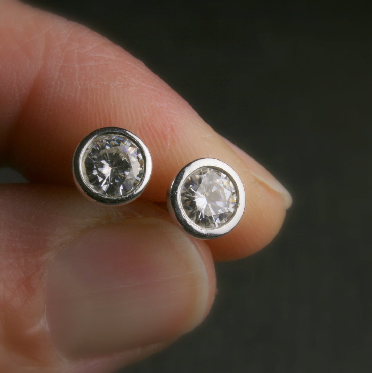 5mm bezel set Moissanite stud earrings in sterling silver. shown being held in a hand for scale