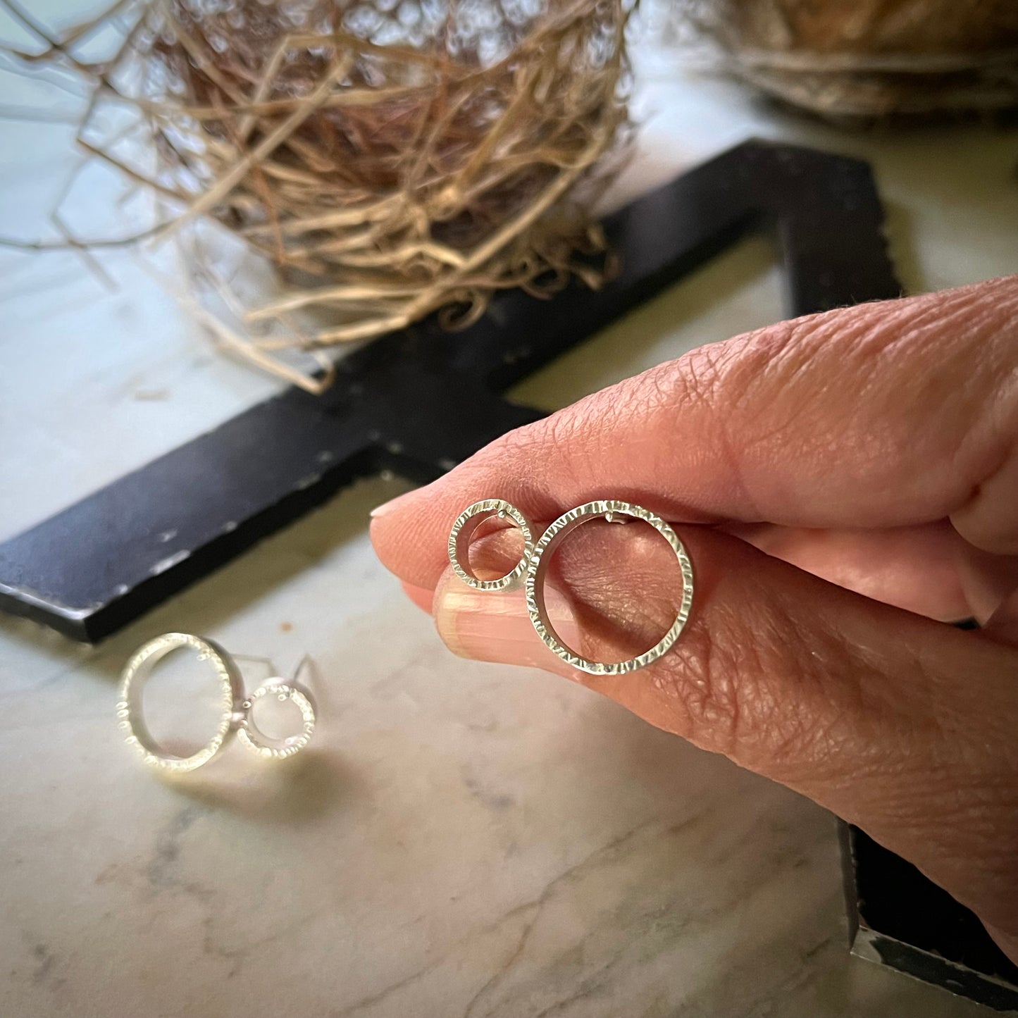 two pair of textured circle hoop earrings. one pair is large and the other small. shown held in a hand for scale