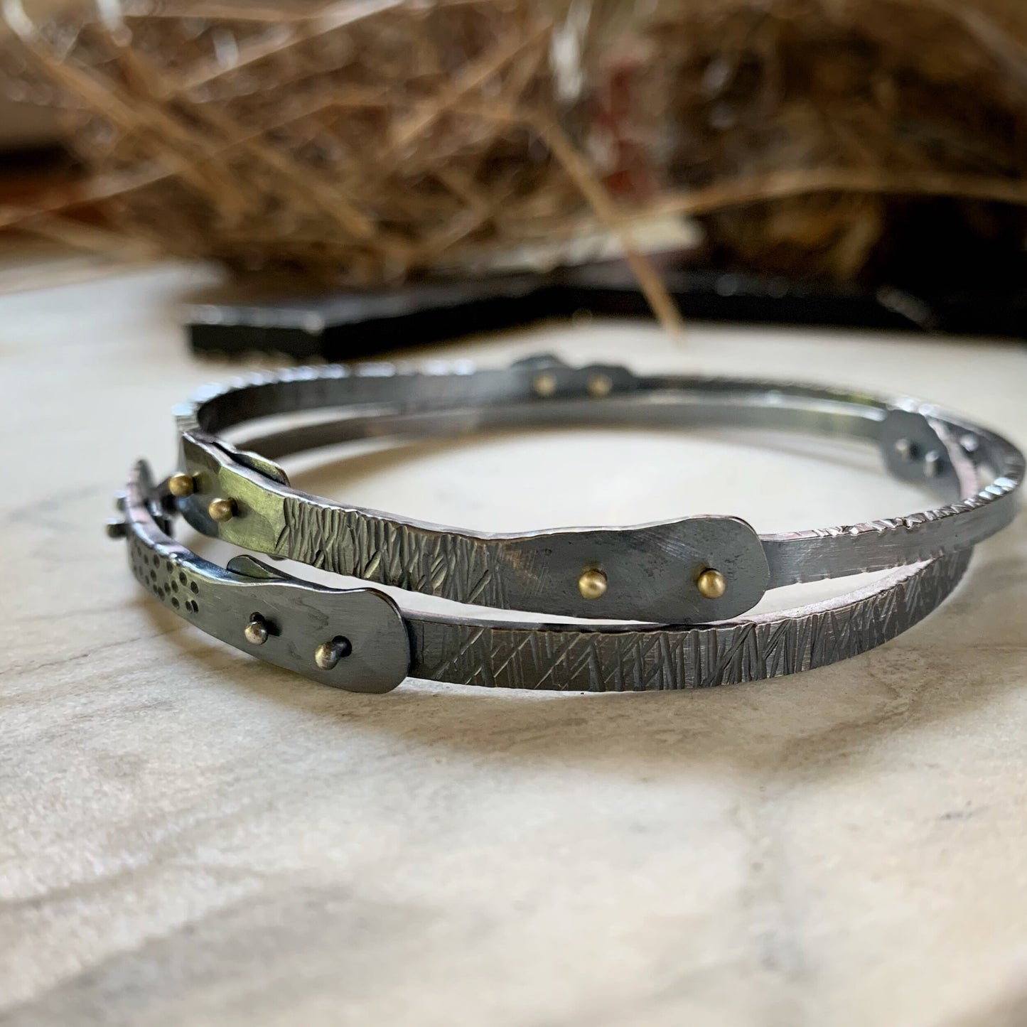Two oxidized silver bangles with silver and gold rivets and texture.