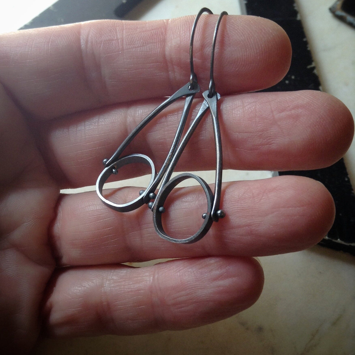 oxidized sterling silver earrings with an industrial look and organic circles. held in a hand for scale