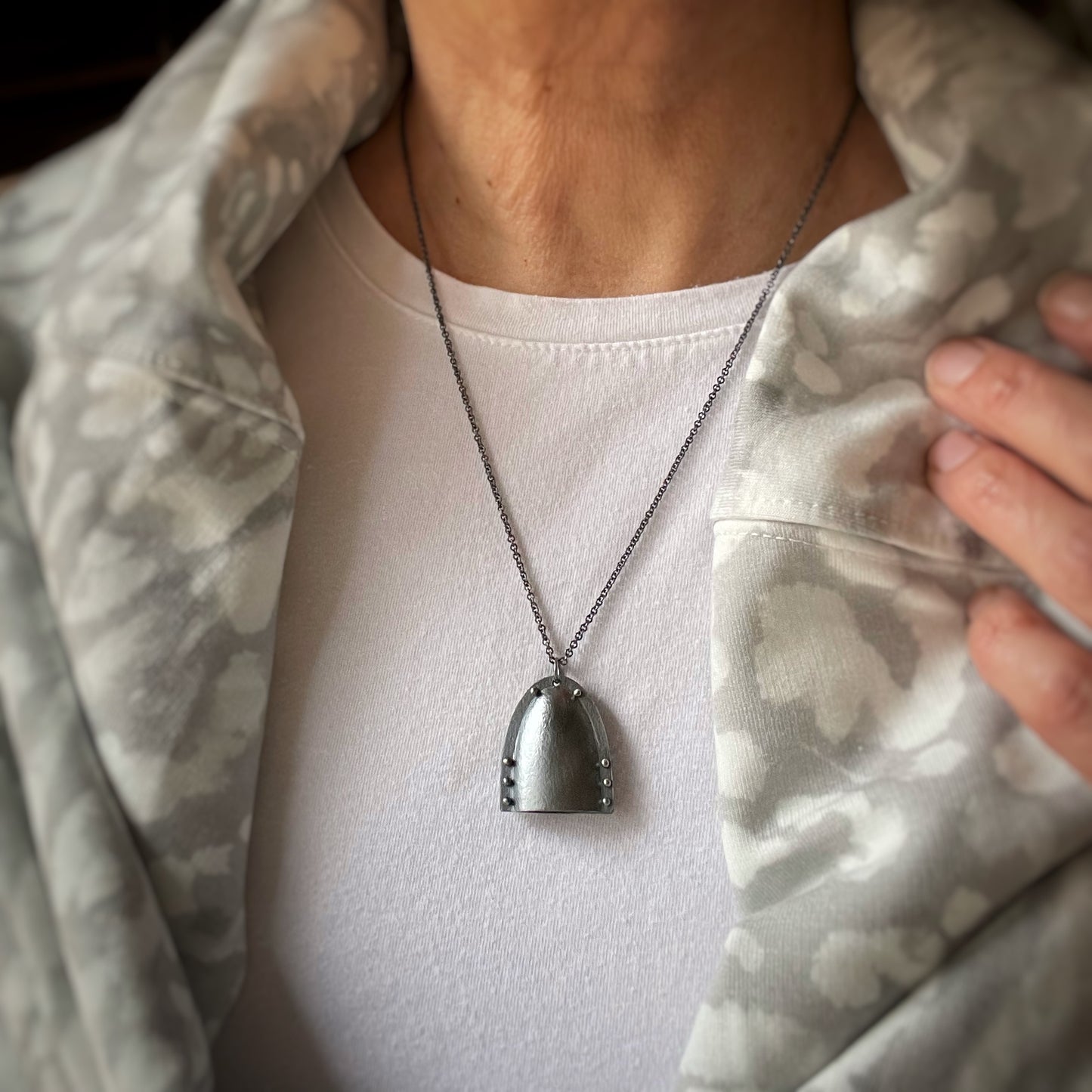 a bell shaped modern pendant with pin rivets in darkened silver. Shown on a model for scale