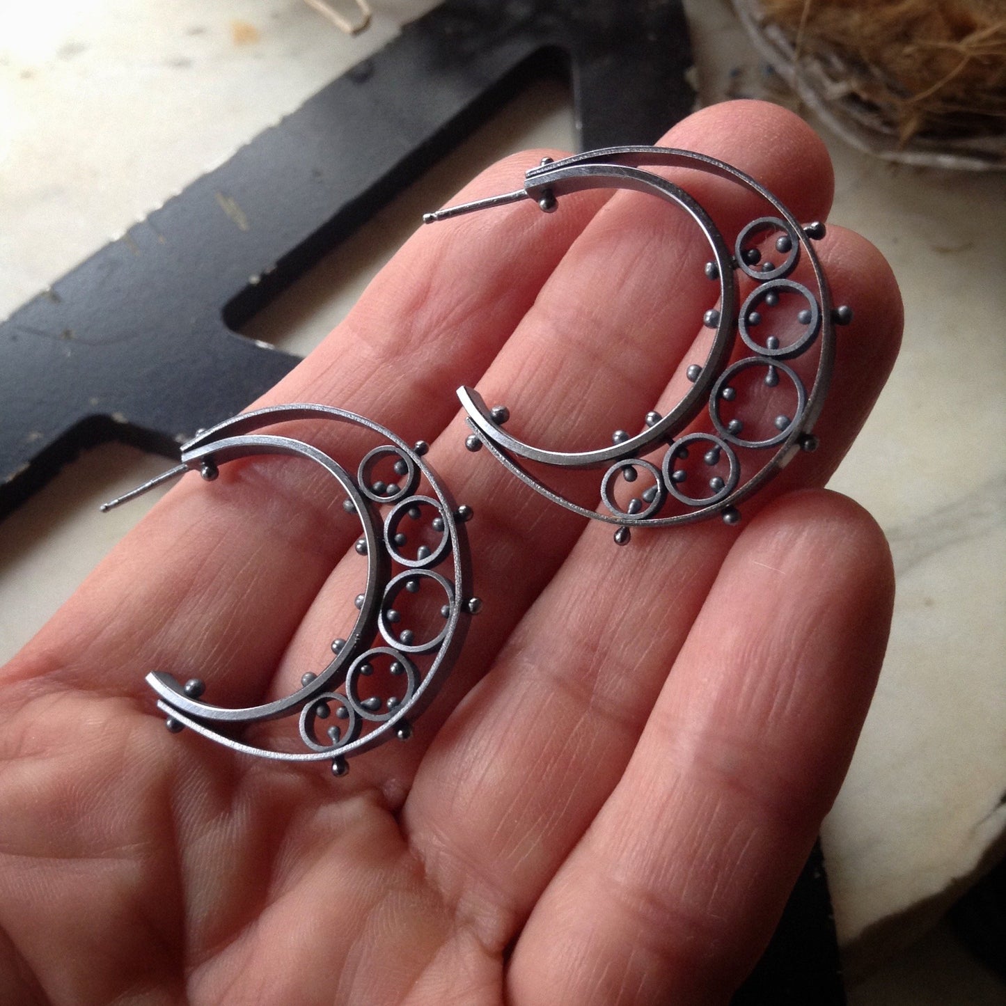 half moon shaped oxidized sterling silver earrings shown in a hand for scale