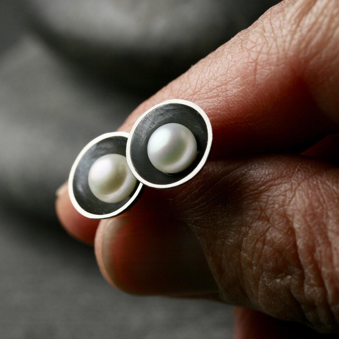 two freshwater pearls set in oxidized sterling silver cups shown in a hand for scale