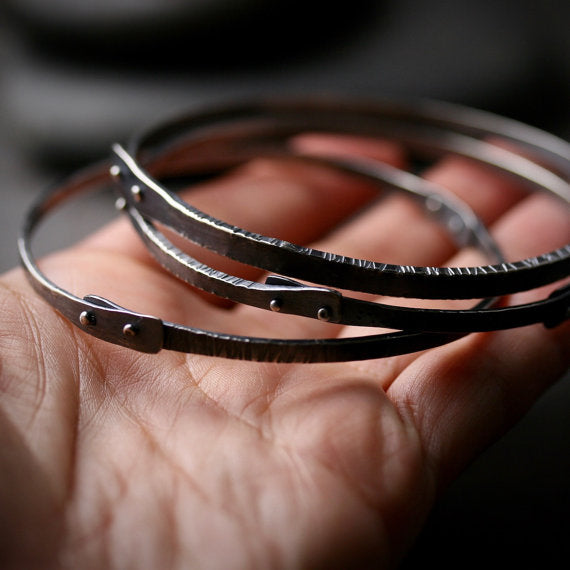 Three oxidized silver bangle bracelets with rivets and texture. Shown on a hand for scale.