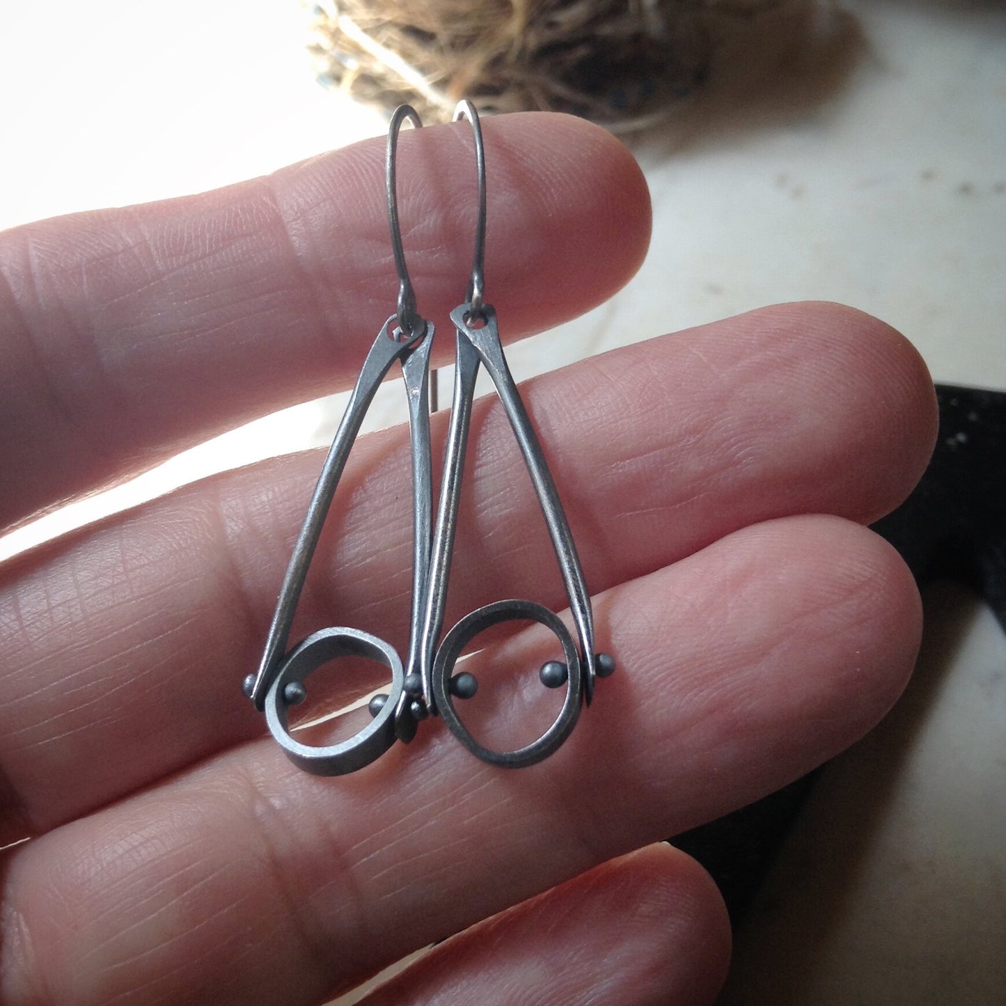 oxidized sterling silver dangle earrings with an industrial look and organic circles held in a hand for sclale