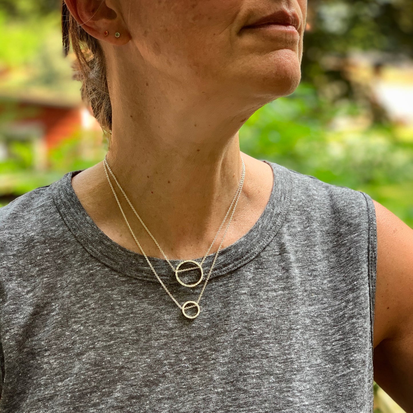 two pendants, one large and one small, in sterling silver. They are circles with a hammered texture and the chain runs through the circle. Shown on a model for scale