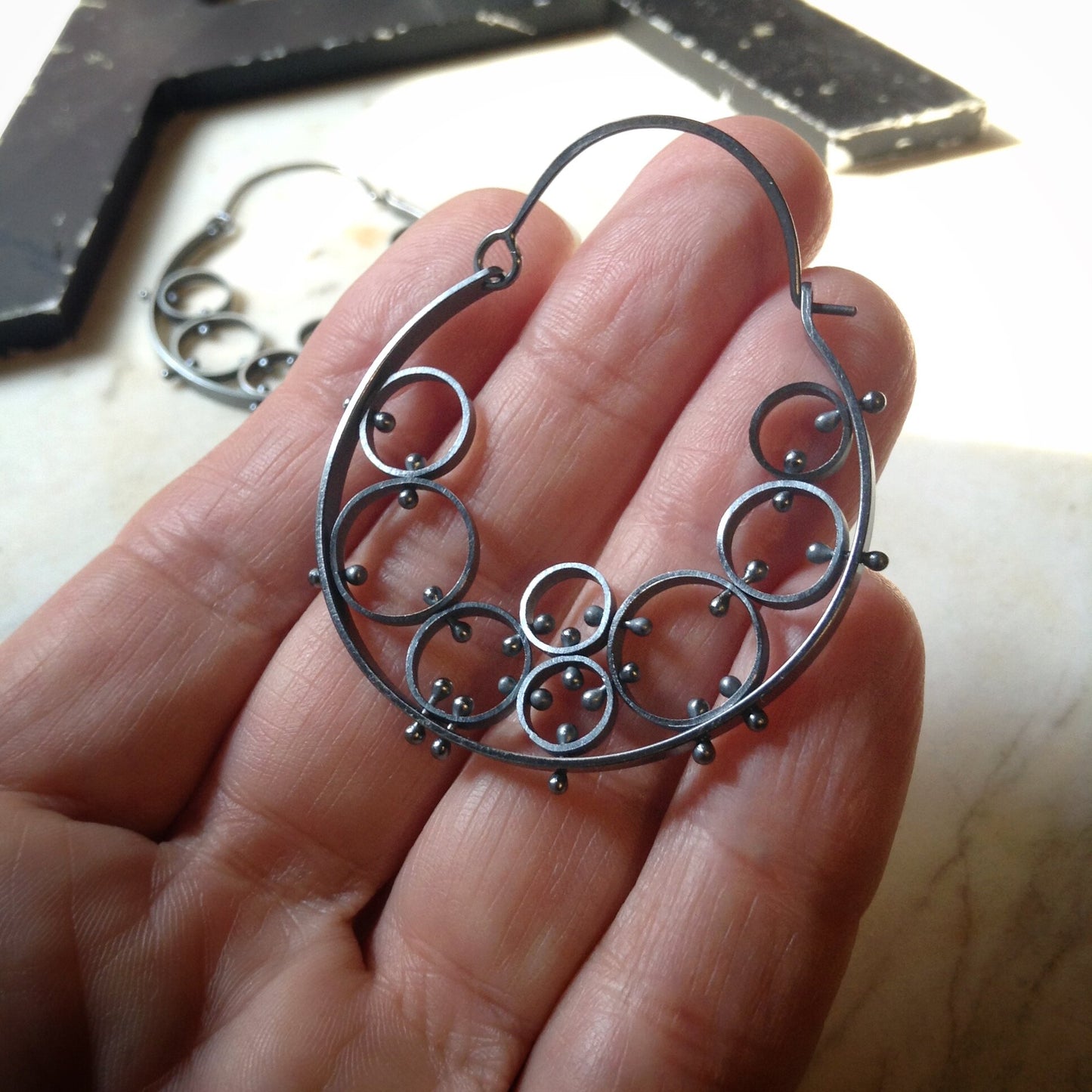 large unique hoop earrings with lots of circles shown on a hand for scale.