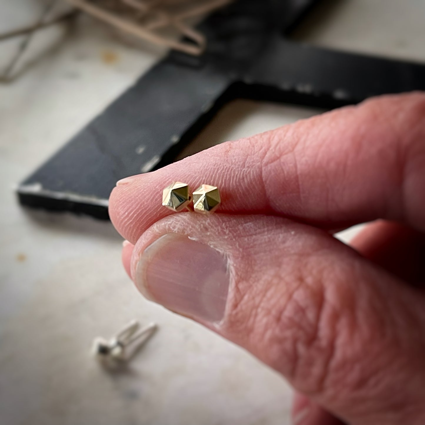 tiny hexagonal stud earrings. A pair in yellow gold is held in a hand for scale
