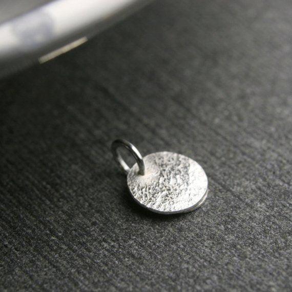 tiny disc with hammered texture showing the back of the pendant