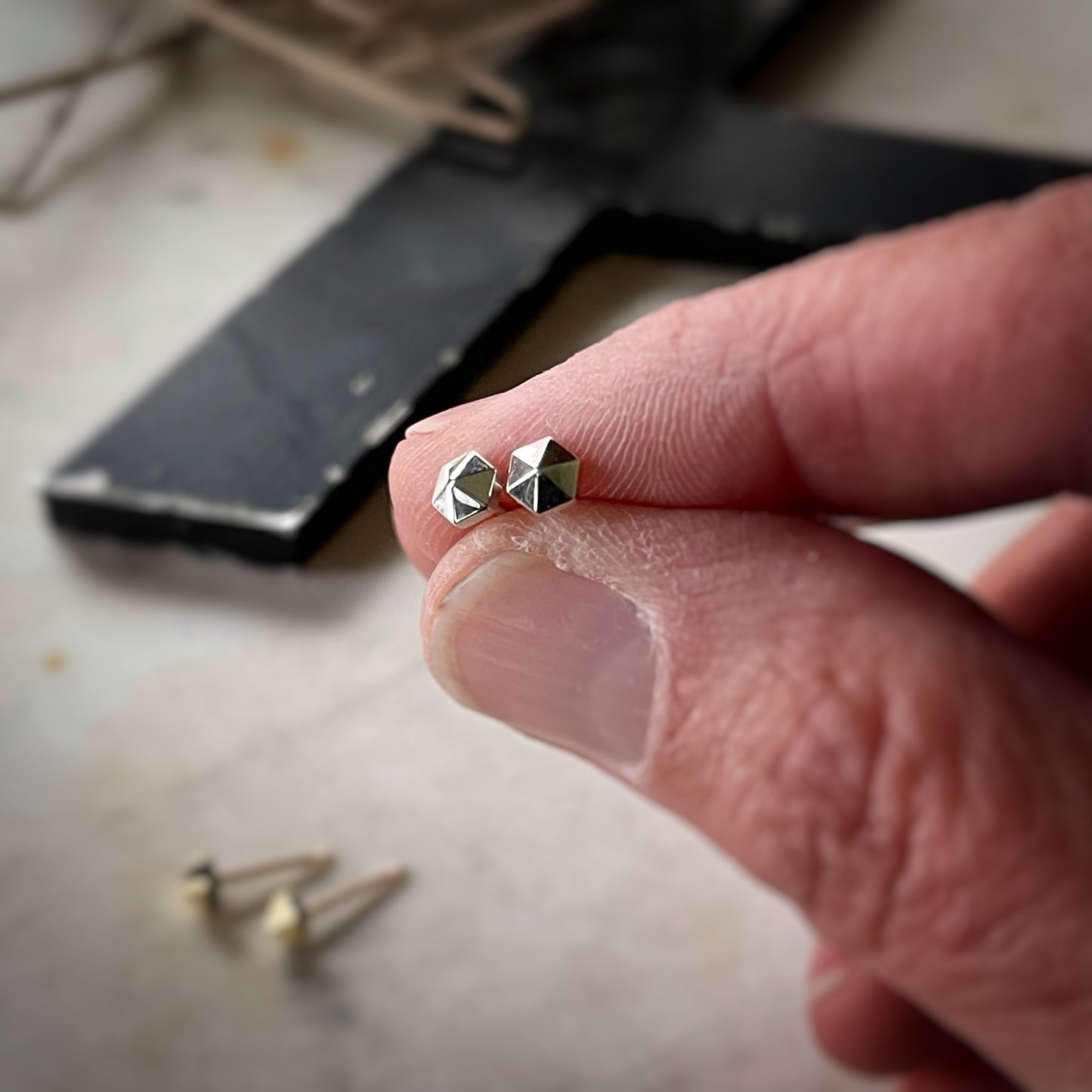 tiny hexagonal stud earrings. A pair in sterling silver is held in a hand for scale