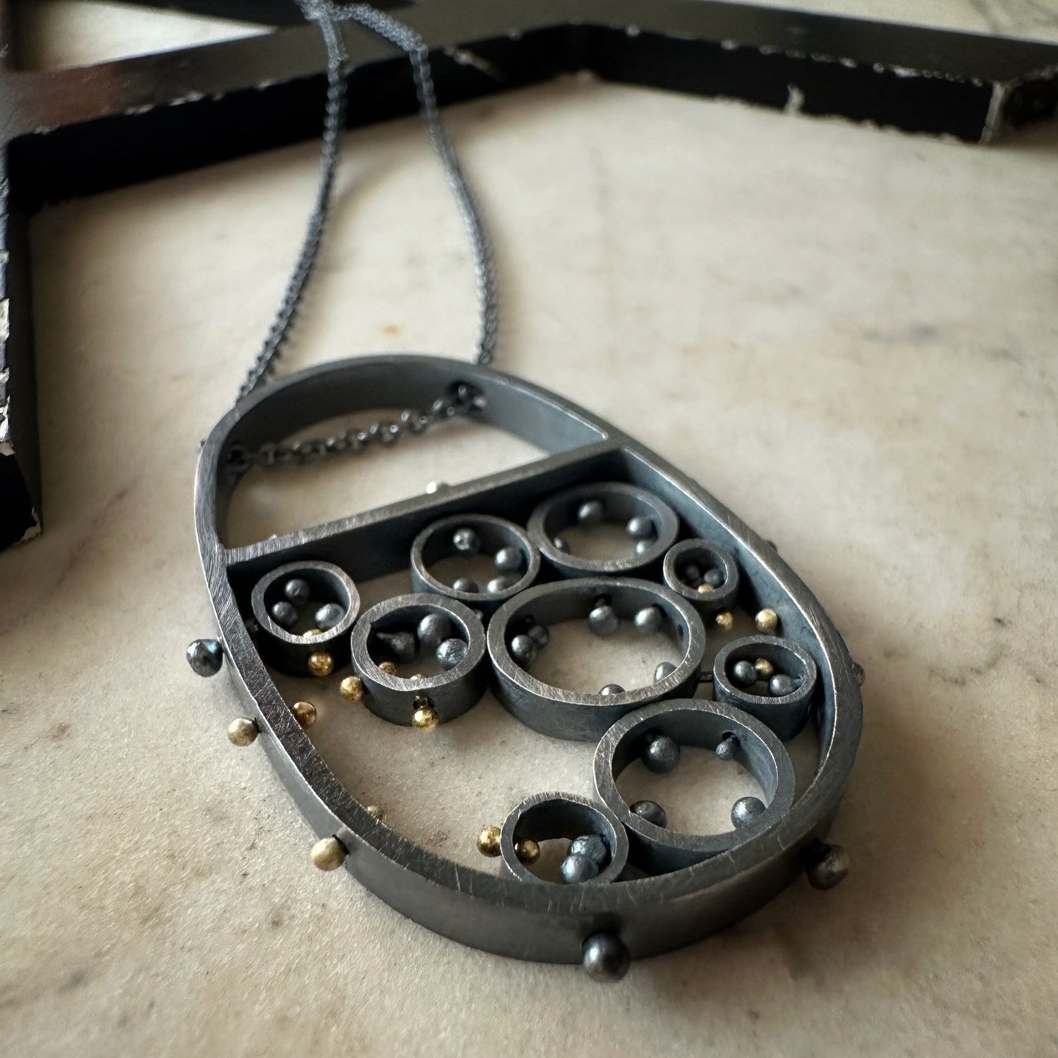 Oxidized sterling silver and gold pendant necklace with cellular circle design and gold rivet details, handmade by Ann Hartley Studio