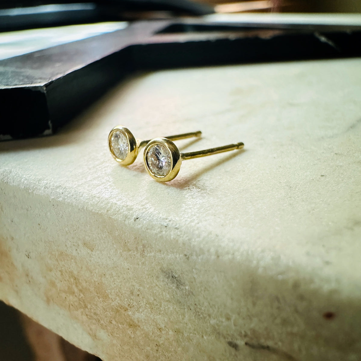 18k yellow gold 3mm Moissanite bezel set stud earrings on a marble background 