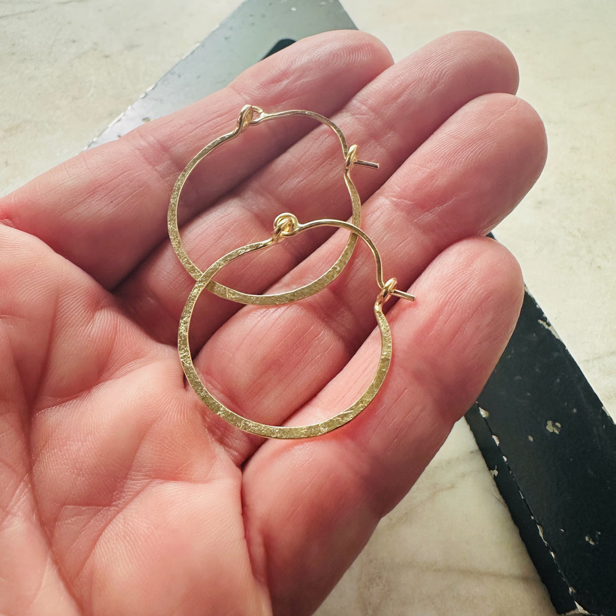 18k yellow gold hammered hoop earrings shown in a hand for scale