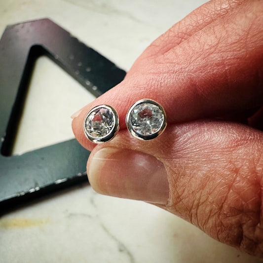 5mm white topaz bezel set stud earrings in sterling silver held in fingers to show scale 