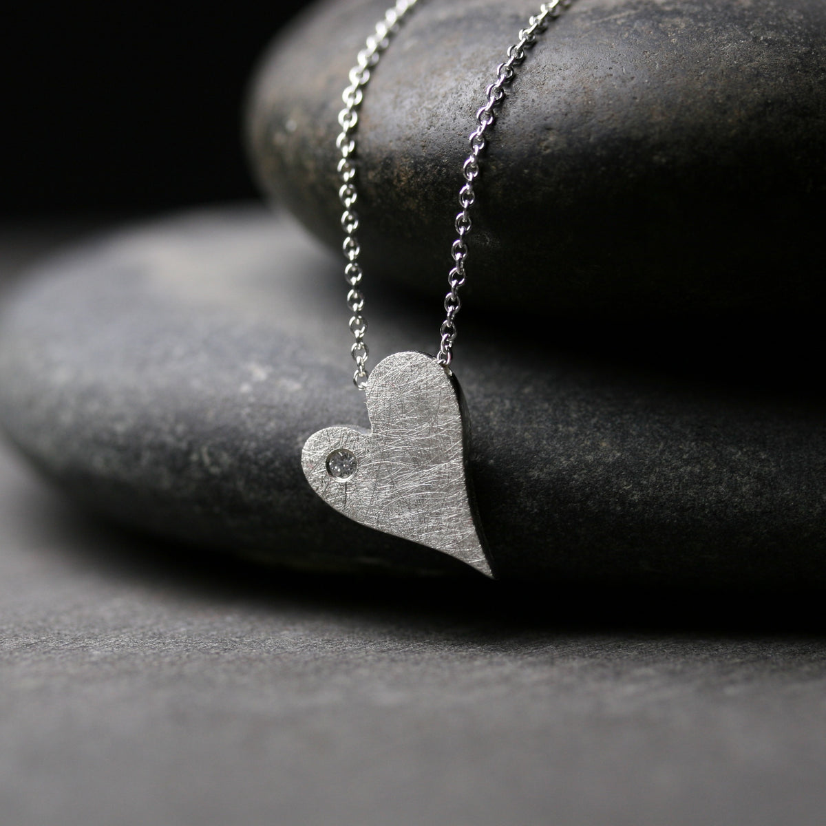 tiny heart shaped pendant with a brushed finish and a small diamond 