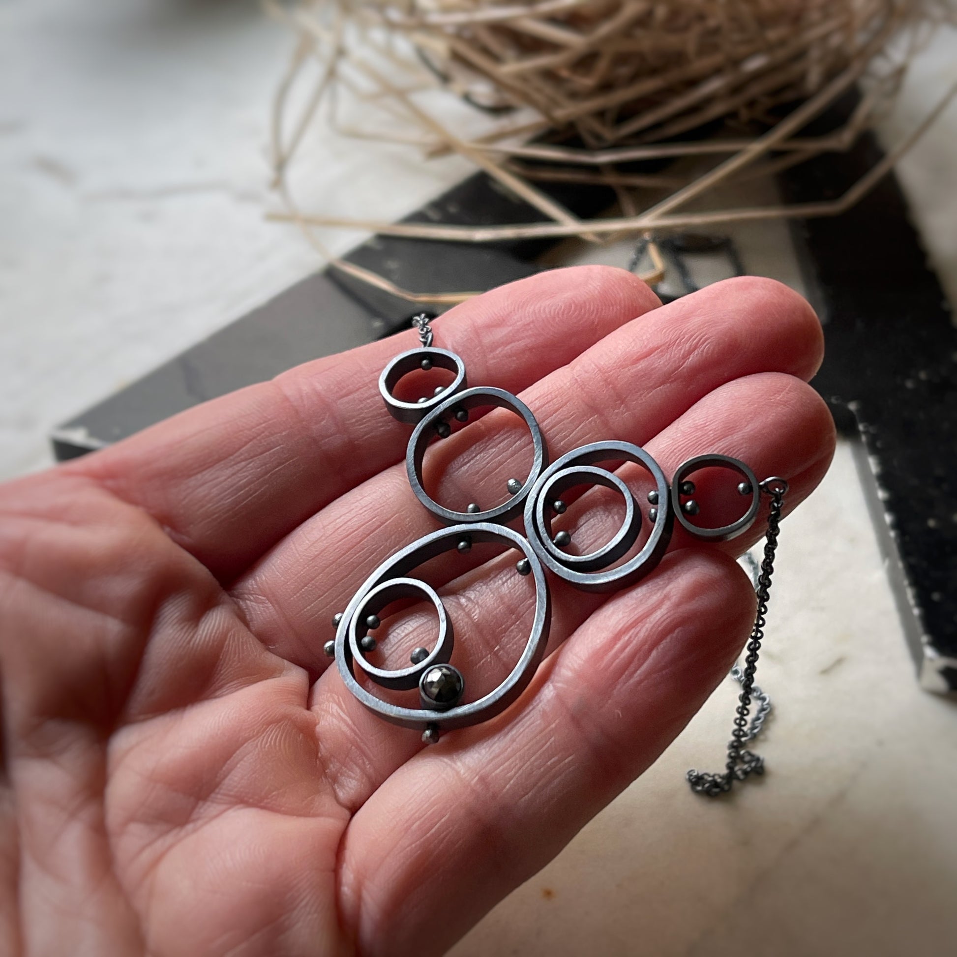 concentric circle modern pendant with rivets and hematite.  Shown on a hand for scale