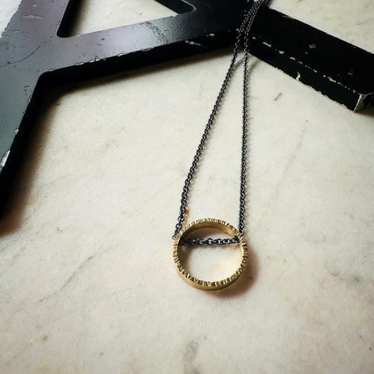 yellow gold hammered texture circle pendant with oxidized sterling silver chain on a marble surface 