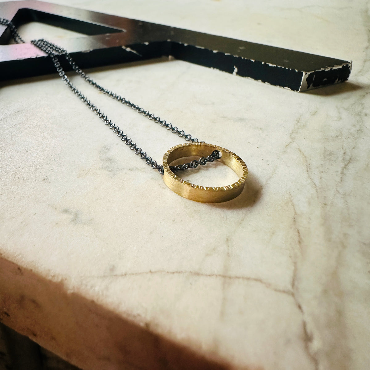 yellow gold hammered texture circle pendant with oxidized sterling silver chain on a marble surface 