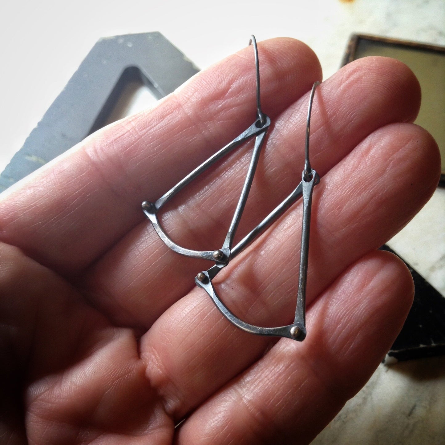 triangle earrings with pinned rivets shown on a hand for scale