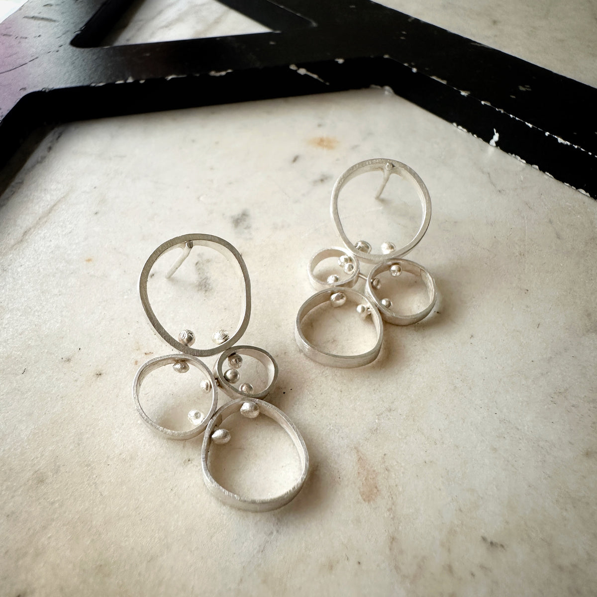 A pair of silver-toned geometric dangle earrings with overlapping circular rings and small bead details, displayed on a light marble surface.