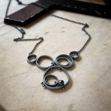 Load image into Gallery viewer, concentric circles held together with rivets and a bezel set hematite pendant
