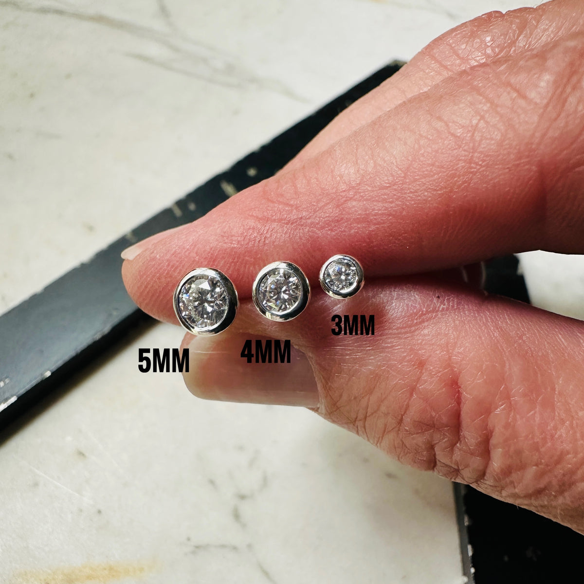 Size comparison between 3mm, 4mm and 5mm being held in a hand for scale sterling silver moissanite studs