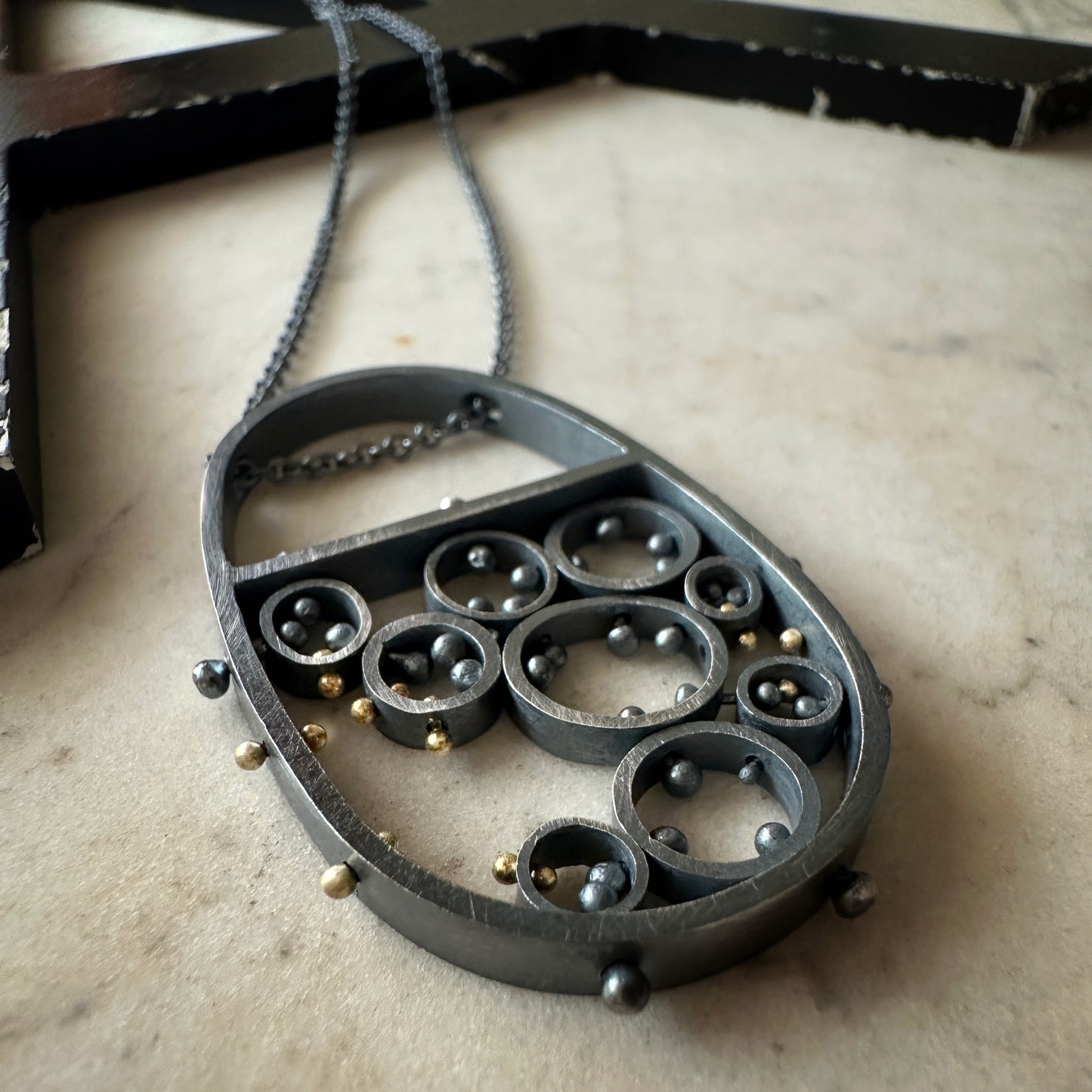 Oxidized sterling silver and gold pendant necklace with cellular circle design and gold rivet details, handmade by Ann Hartley Studio