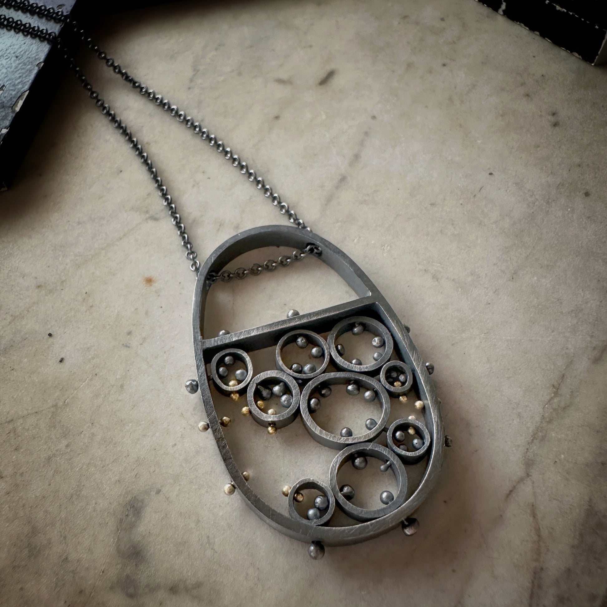 Oxidized sterling silver and gold pendant necklace with cellular circle design and gold rivet details, handmade by Ann Hartley Studio