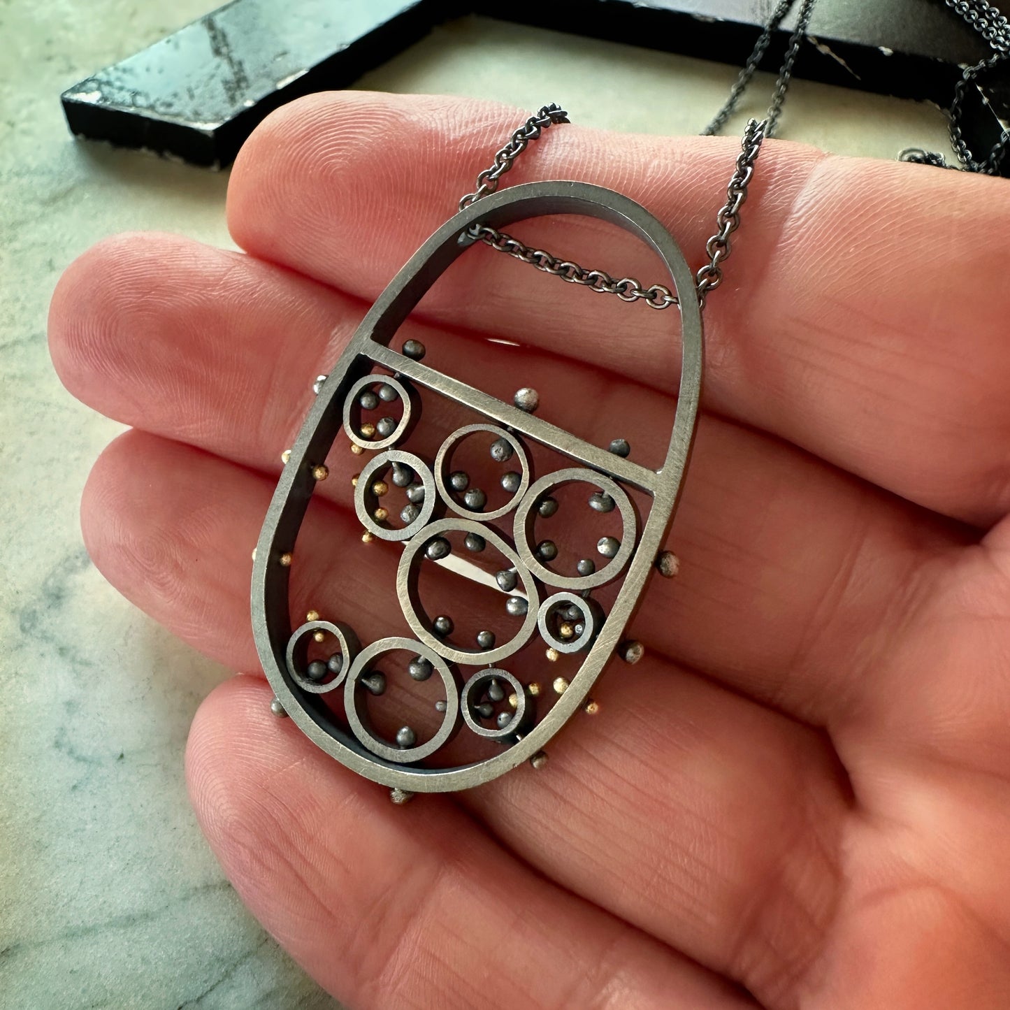 Oxidized sterling silver and gold pendant necklace with cellular circle design and gold rivet details, handmade by Ann Hartley Studio