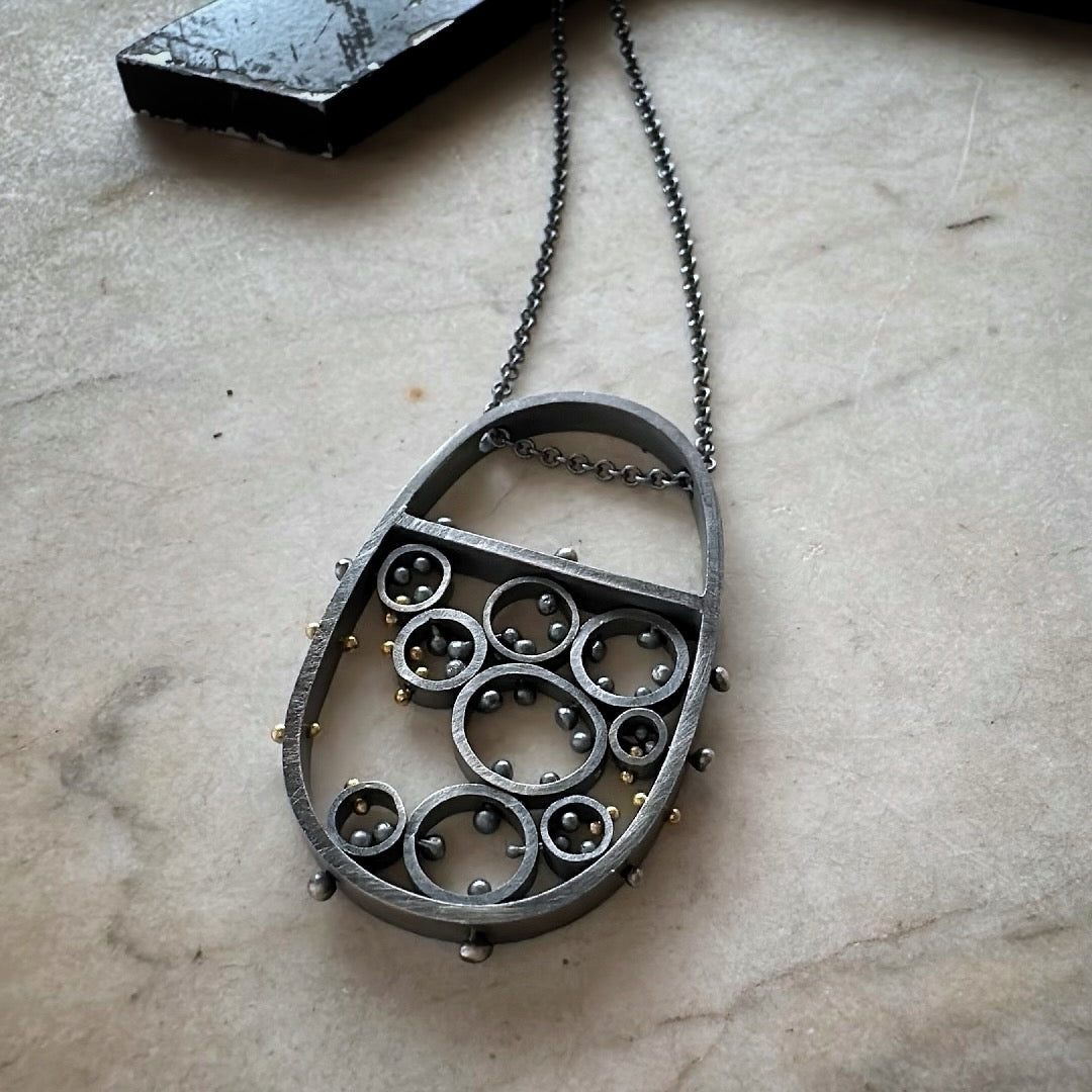 Oxidized sterling silver and gold pendant necklace with cellular circle design and gold rivet details, handmade by Ann Hartley Studio