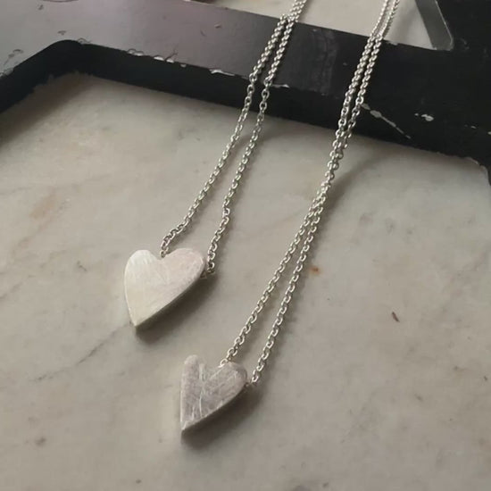 two sterling silver heart pendants in sterling silver on a marble surface 