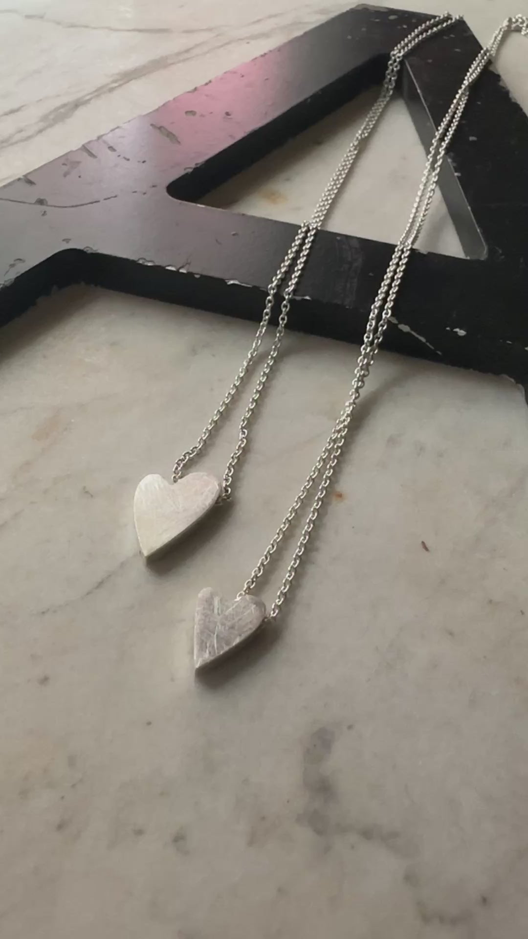 two sterling silver heart pendants in sterling silver on a marble surface 