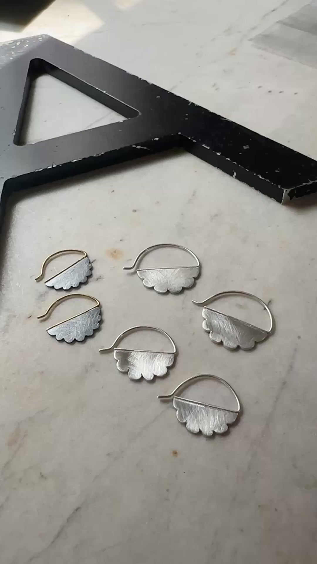two pair of silver cloud shaped hoop earrings with scalloped edges, displayed on a light beige marble surface next to a black wooden block.