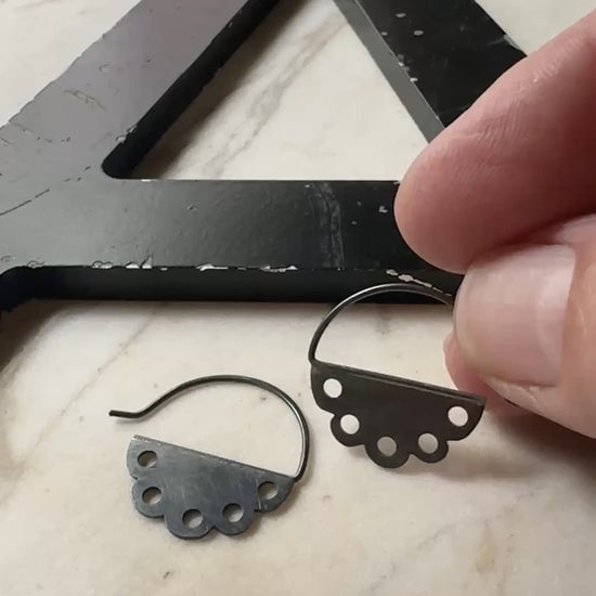 a video of a hand holding an oxidized silver pair of scalloped edge hoop earrings