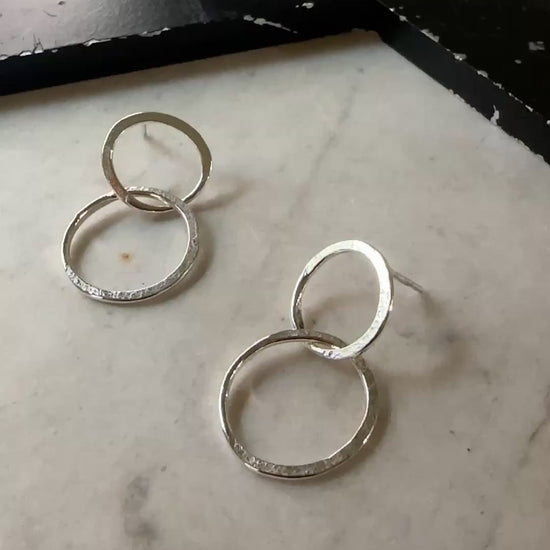 A pair of textured silver hoop earrings resting on a light beige marble surface.