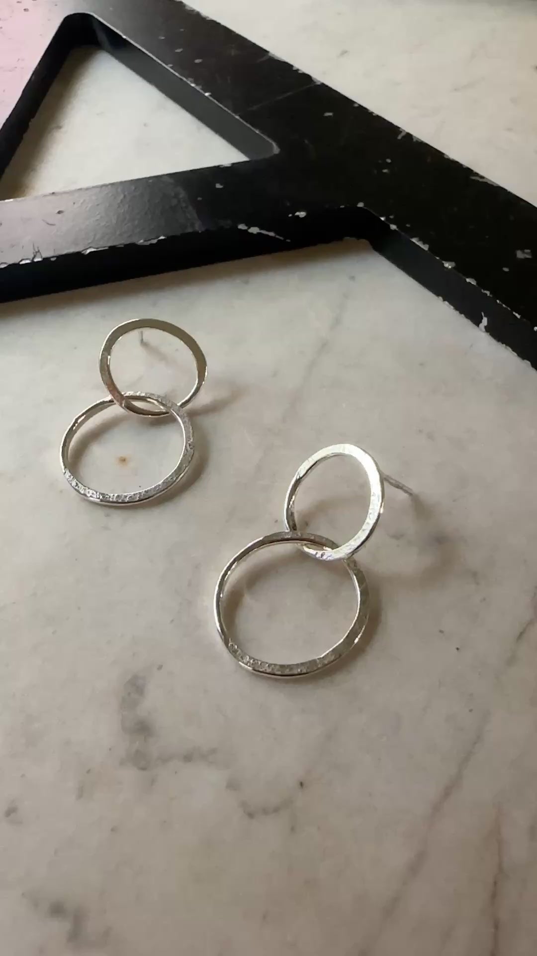 A pair of textured silver hoop earrings resting on a light beige marble surface.