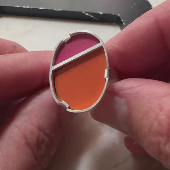 a sterling silver oval ring with a top half in bright pink formica and bottom half in bright orange 