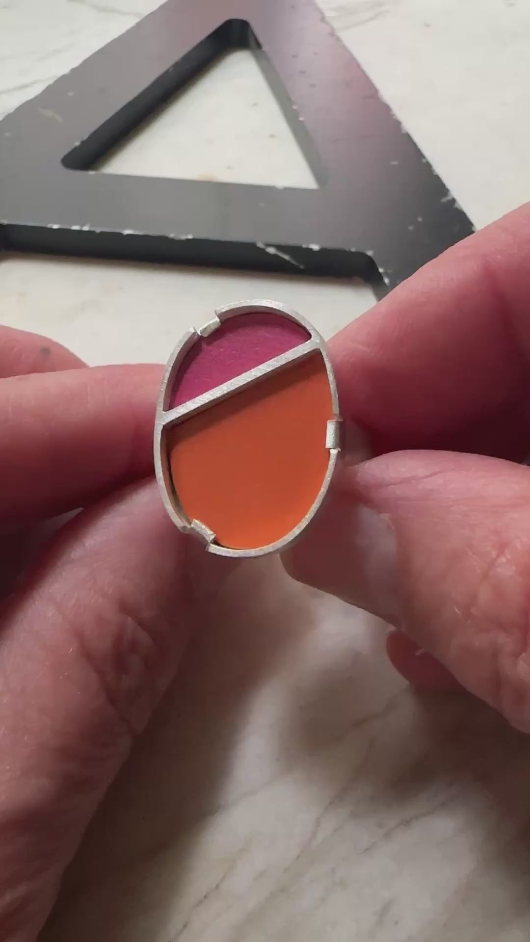 a sterling silver oval ring with a top half in bright pink formica and bottom half in bright orange 