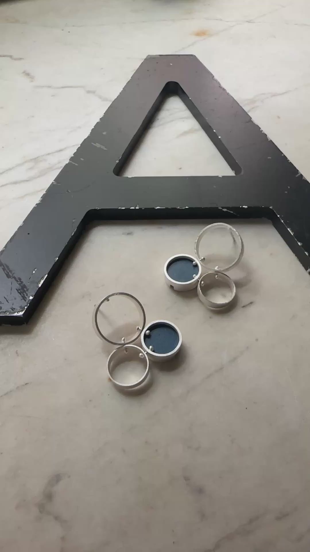 A pair of silver post  earrings with cellular drop elements featuring small round blue formica, displayed on a light marble surface.