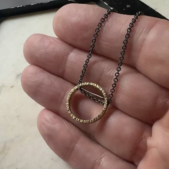 yellow gold hammered texture circle pendant with oxidized sterling silver chain on a marble surface 