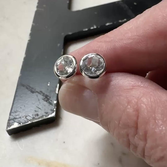 a pair of 6mm white topaz bezel set stud earrings resting on a marble surface